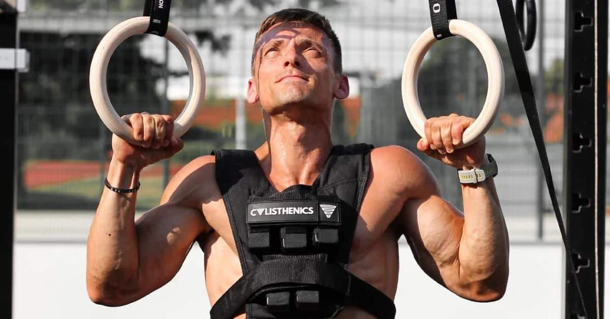 Strong man is doing weighted pull-ups with a weighted vest and gymnastic rings
