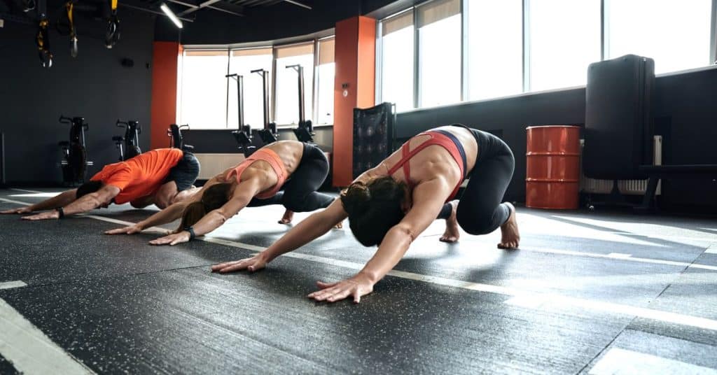 A man and two women are doing the downward facing dog exercise