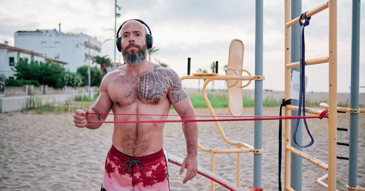 Bald man with beard and headphones is doing a warm-up exercise with a resistance band